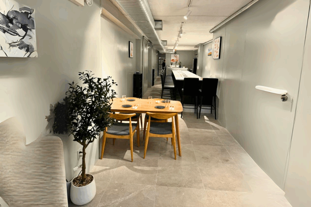 The narrow SourAji dining room with a wooden four-top, olive tree and the long sushi counter behind
