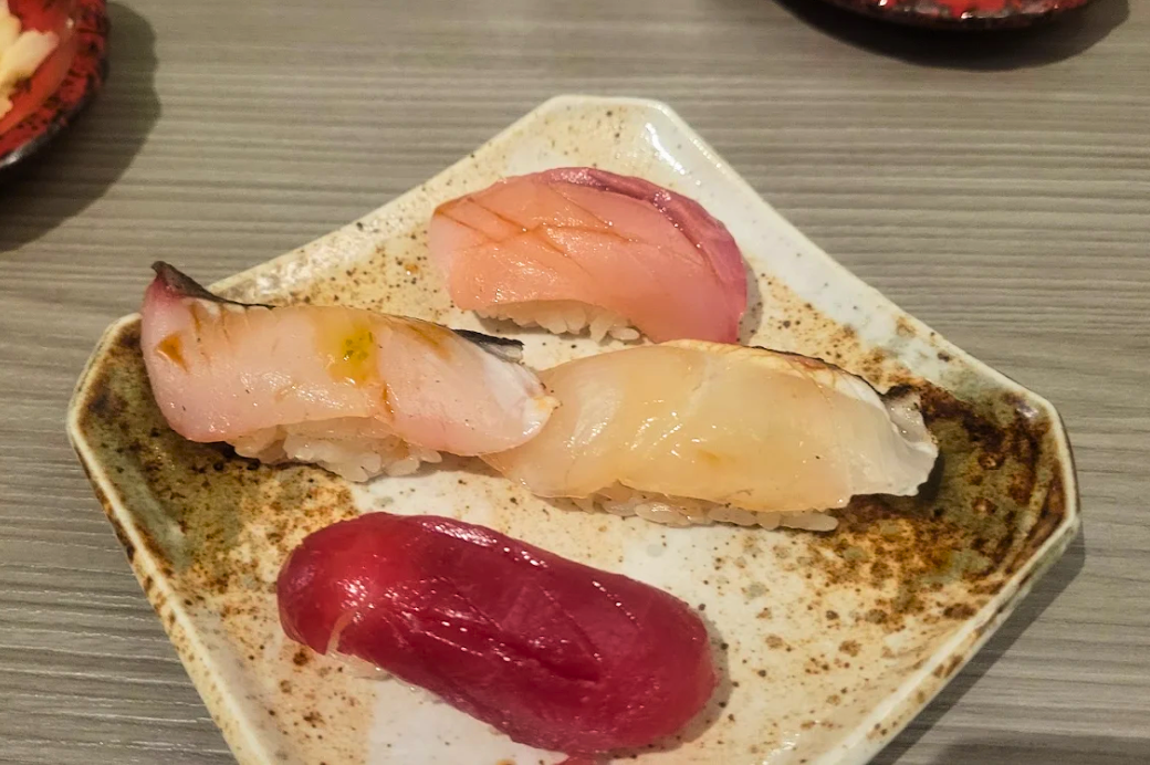Four pieces of SourAji nigiri on a speckled ceramic plate including yellowtail, aburi and lean tuna