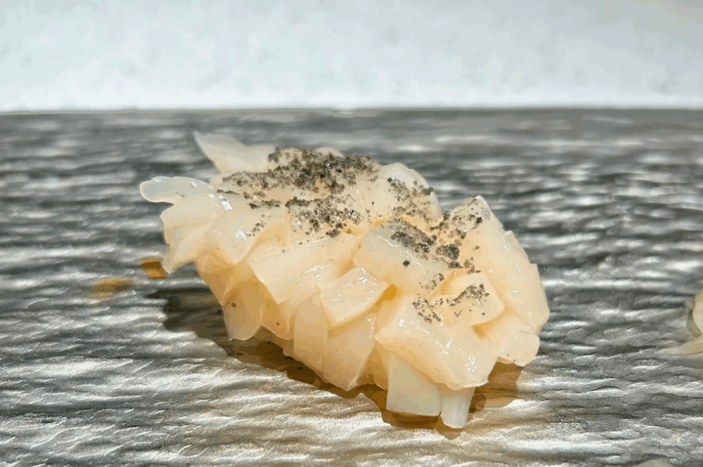 Close-up of Hokkaido scallop nigiri topped with shaved black truffle