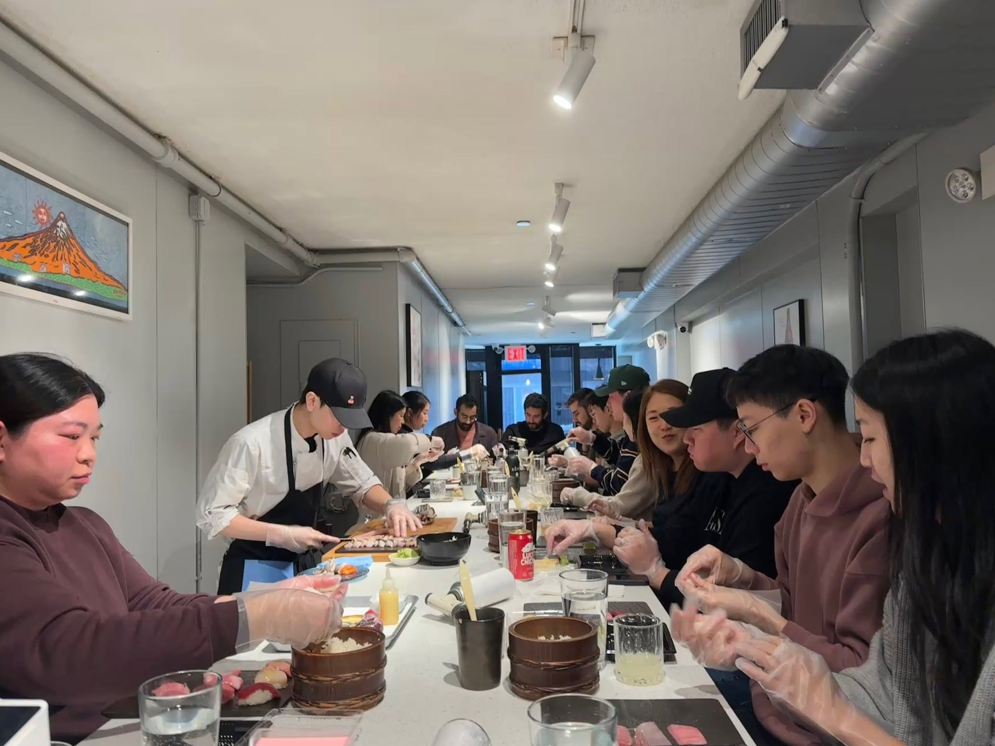 A full counter of guests wearing gloves shaping their own nigiri during a SourAji sushi-making class