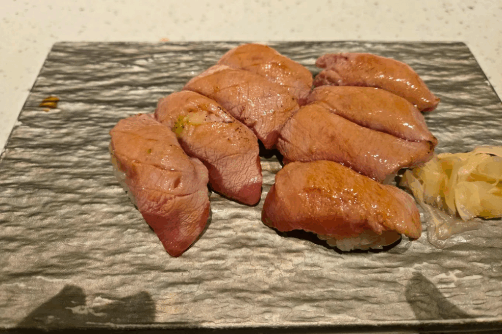Seven pieces of seared A5 wagyu nigiri arranged on a textured stone slab with pickled ginger
